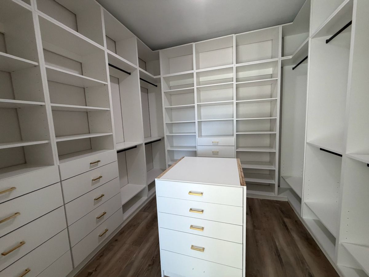 White walk-in closet island with brass pulls and open shelving