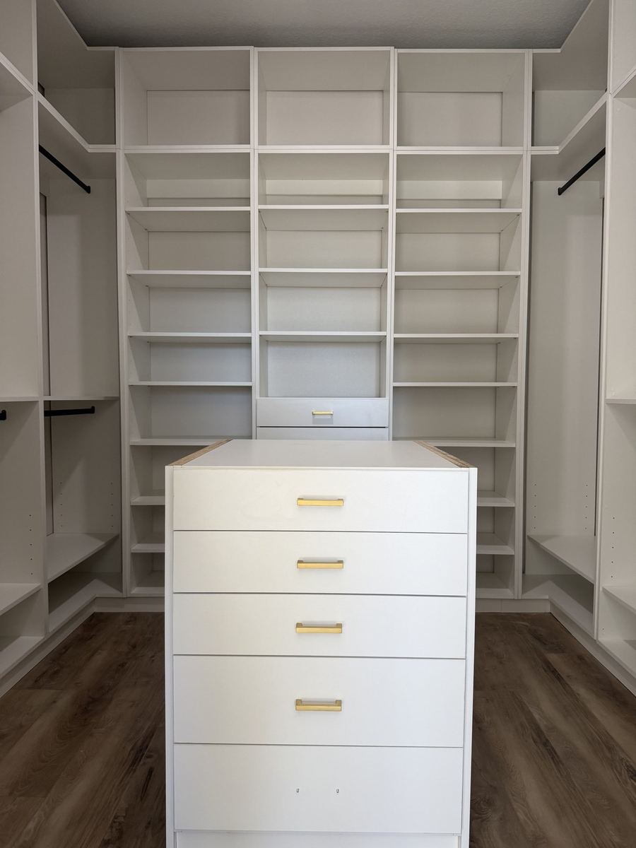 White walk-in closet built around a brass handled drawer island