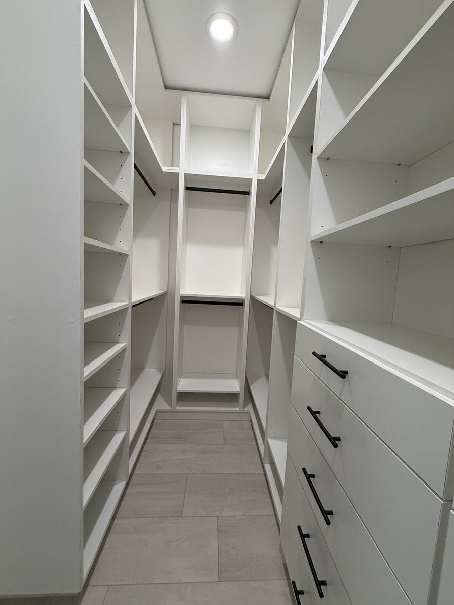 Narrow white walk-in closet with matte black rods and a drawer bank