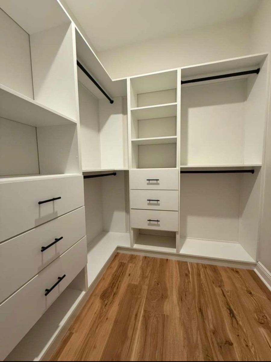 White walk-in closet with matte black rods over warm wood flooring